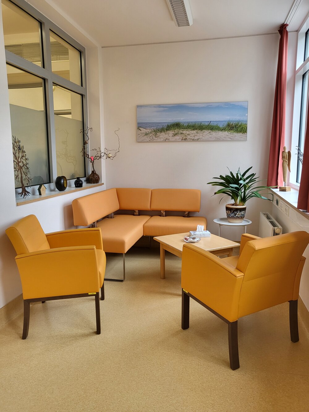 Das Wohnzimmer auf der Palliativstation ist mit einer gemütlichen Eckcouch in Ocker und Sesseln ausgestattet.